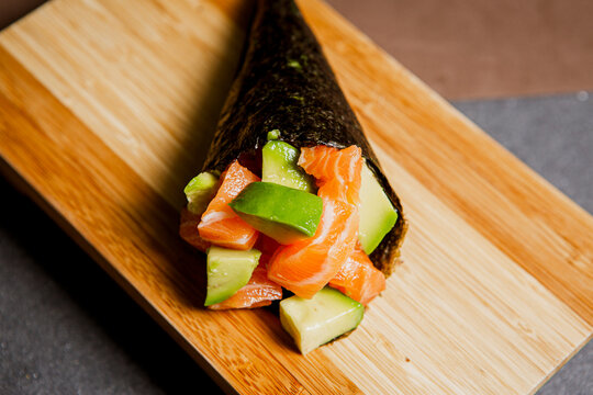 
Sushi temaki freshly prepared with salmon and avocado. Japanese food in a wooden background. Fish and avocado slices. Top view with Copy Space.