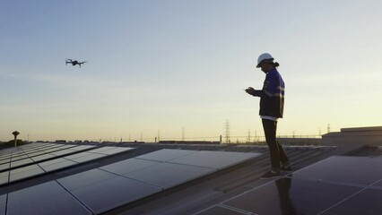 Specialist technician professional engineercontrol drone checking top view of installing solar roof panel on the factory rooftop under sunlight. Engineers holding tablet check solar roof.