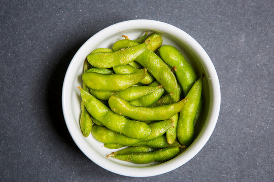 Raw organic beans edamame in a white bowl. Black background. Top view and copy space.