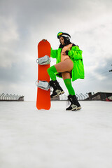 Young beautiful woman with a slim body in an erotic suit posing with a snowboard on a ski slope