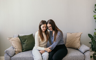 Obraz premium Psychological assistance to women. Domestic violence. Two women are sitting on the couch and hugging. Supportive hugs