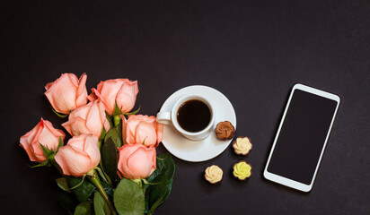 Fototapeta na wymiar Pink roses, coffee cup, smartphone and chocolate candies on dark background