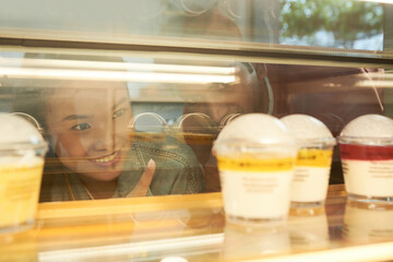 Smiling young couple looking at dairy desserts in cafe showcase