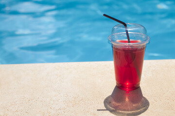 Refreshing juicy drink in a takeaway plastic glass by the pool on a hot day in a hotel on vacation 