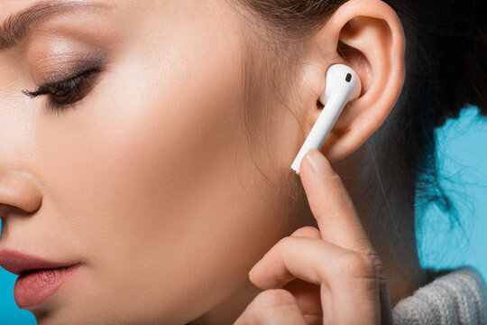Cropped view of woman using wireless earphone isolated on blue.