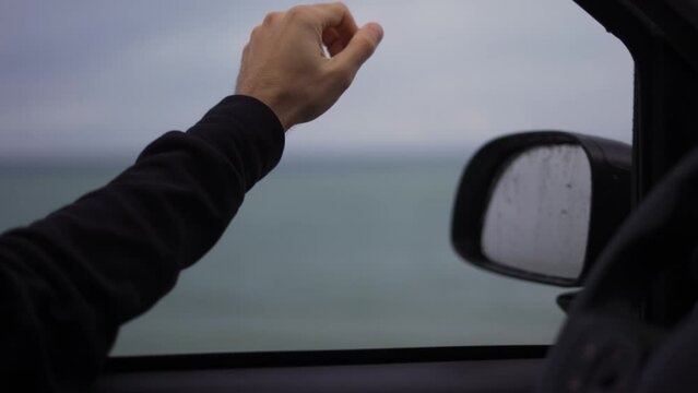 A man's hand is catching the rain out while driving a car on a rainy day