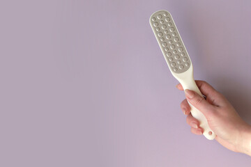 pink foot grater in a woman's hand on a gray background, space for text