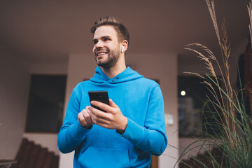 Cheerful male in electronic headphones enjoying music podcast resting at city street, joyful...