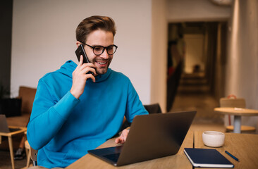 Happy hipster guy editing content vlog on laptop computer calling to influence colleague for...