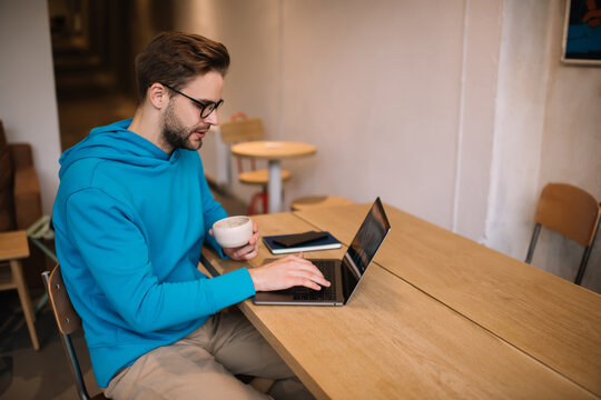 Skilled Caucasiasn freelancer browsing web design on modern laptop computer, young IT professional in optical spectacles for provide eyes protection creating program code during remote working