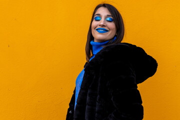 smiling woman with closed eyes and blue make-up on yellow background