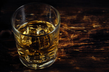 Glass chilled whiskey with ice cubes on wooden background.
