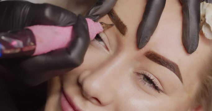 A professional needle applies tattoos skin eyebrow area. Girl's face close up.