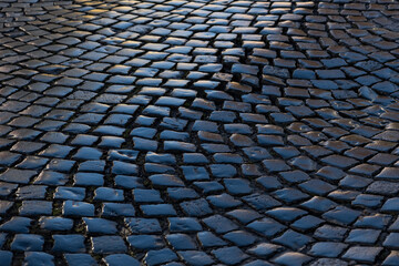 Cobblestone street in old town  in Germany. Wet shiny historic basalt ashlars or blocks reflecting blue sky and sunshine after rain. Wheathered pavement background with typical surface and structure.