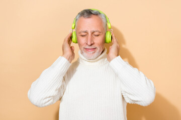 Portrait of attractive dreamy grey-haired man enjoying listening soul jazz isolated over beige...