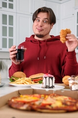 Overweight man eating tasty croissant at table in kitchen