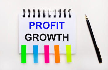 On a light background, a pen, a notebook with the text PROFIT GROWTH and bright stickers.