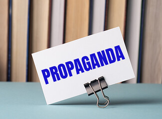 A white card with the text PROPAGANDA stands on a clip for papers on the table against the...