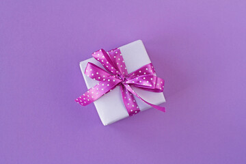 Gift box with white polka dot ribbon bow on purple background