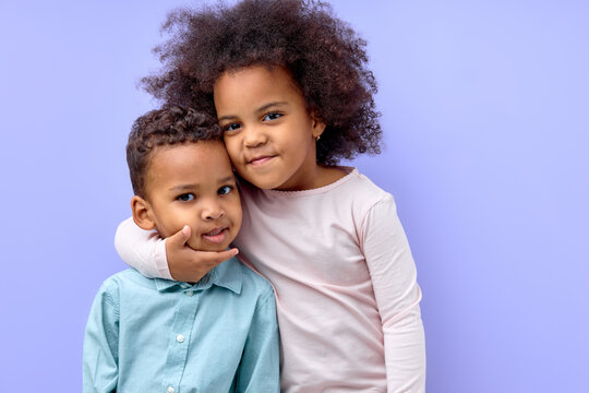 Cute black girl hugging little brother, showing love and affection, purple studio background. Happy loving afro american siblings in casual wear embracing and smiling at camera. family, love