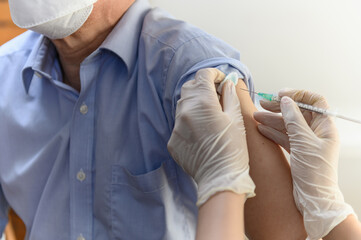 Close up hand of Asian woman nurse injecting covid-19 vaccine to senior Thai man patient wearing...