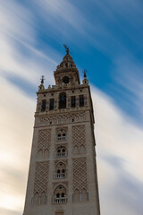 Fototapeta na wymiar A Long exposure during the day with a view on the historic La Giralda tower in the heart of Seville with moving clouds. This iconic landmark can be seen throughout the city