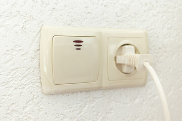 white socket with plug and light switch on an empty wall with space for text