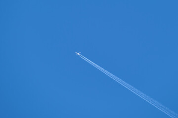 Distant passenger jet plane flying on high altitude on clear blue sky leaving white smoke trace of contrail behind. Air transportation concept