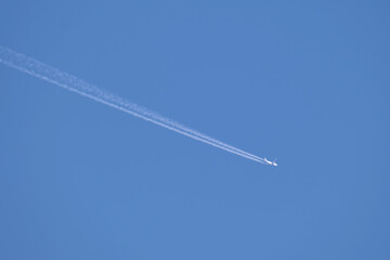 Distant passenger jet plane flying on high altitude on clear blue sky leaving white smoke trace of contrail behind. Air transportation concept