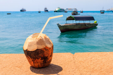 Fresh tropical coconut cocktail with drinking straw by ocean in Stone Town, Zanzibar, Tanzania