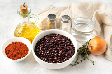 Ingredients for cooking a bean dish. Legumes, onions, salt, pepper, paprika, olive oil and thyme sprigs on a light gray kitchen table