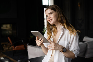 A female freelance designer works in a hotel workplace uses a tablet, communicating with a client.