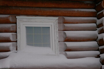 a fragment of the wall of a wooden house in the snow made of timber with a snow-covered window