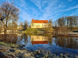 Obraz premium Lutheran church and its reflection on the surface of a reservoir in the Latvian village of Aizpute on a sunny autumn day 2021