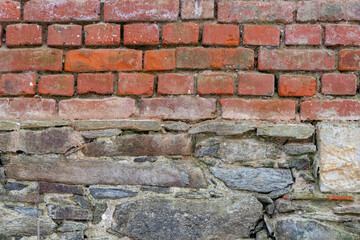 Old red brick wall background texture. Dirty rough backdrop of a building facade. Pattern of small weathered masonry structure. Vintage house exterior with different stone materials.