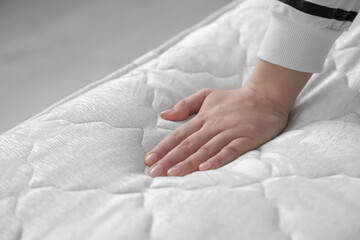 Woman touching soft white mattress indoors, closeup