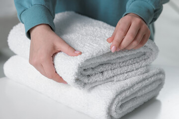 Woman touching soft white towel indoors, closeup