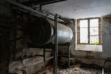 Big old rusty water tank in the basement of an abandoned building. Weathered steel tubes inside in a dirty small room. Important supply in a big house.
