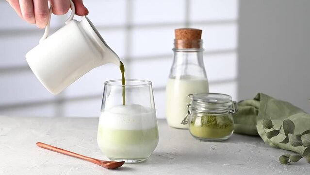 Green matcha latte in a glass on a gray background with morning shadows from the window, a bottle of milk and tea powder The concept of a vegan drink, superfoods and healthy   food
