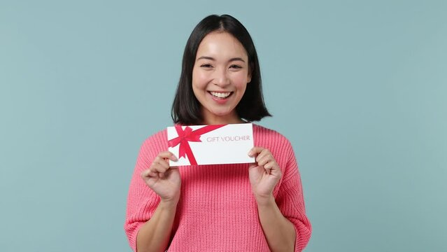 Surprised young woman of Asian ethnicity 20s wears pink shirt pointing finger on gift certificate voucher for store doing winner gesture isolated on plain pastel light blue background studio portrait