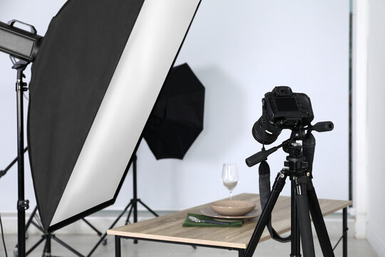 Table with stylish dinnerware in front of camera and professional lighting equipment indoors. Photo studio set