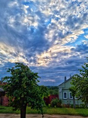 A small house in the village against the backdrop of a beautiful sky with clouds and sun rays