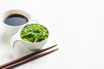 Green wakame. Seaweed salad and soy sauce in bowl.