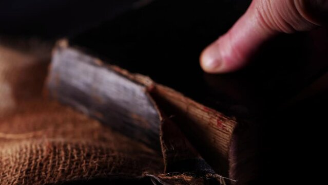Hand opens old worn book on hessian sack and dark smoke background