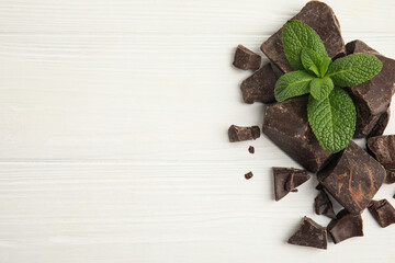 Tasty dark chocolate pieces with mint on white wooden table, flat lay. Space for text