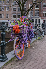 Fototapeta na wymiar Bicycle decorated with colorful flowers parked on the canal bridge. Amsterdam, the Netherlands. 