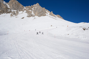 Rodzina zjeżdżająca na nartach. W tle ośnieżone szczyty górskie. Ratrakowane białe stoki.