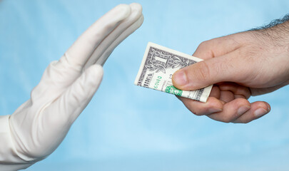 man's hand is giving a dolar to a hand in white surgical glove, nurse or doctor. the hand in glove is refusing the money. corruption in medicine field. pandemic times. blue medicinal background.