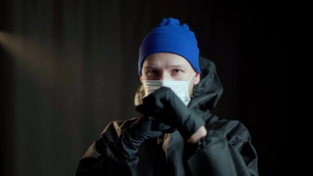 A man in a black medical suit of chemical protection and a white respirator and in black medical gloves and a blue hat delivers boxing punches