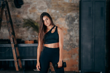 Young woman posing at the camera with dumbbells in her hands.